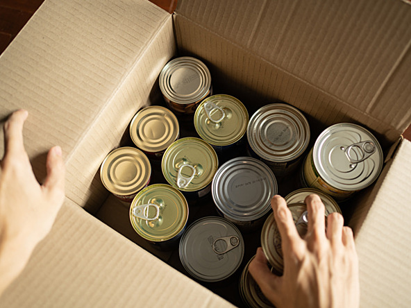 person stockpiling tins of food in cardboard box